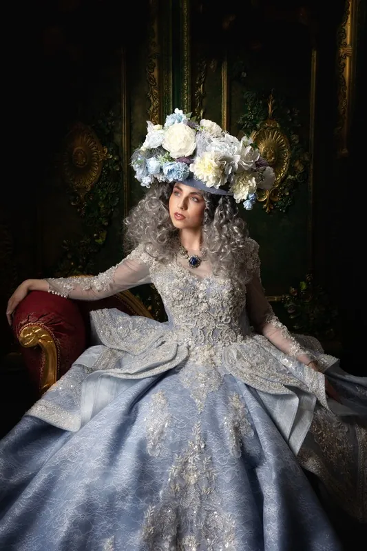 Vicky im hellblauen Barockkleid mit Blumenkrone auf einem roten Samtsessel