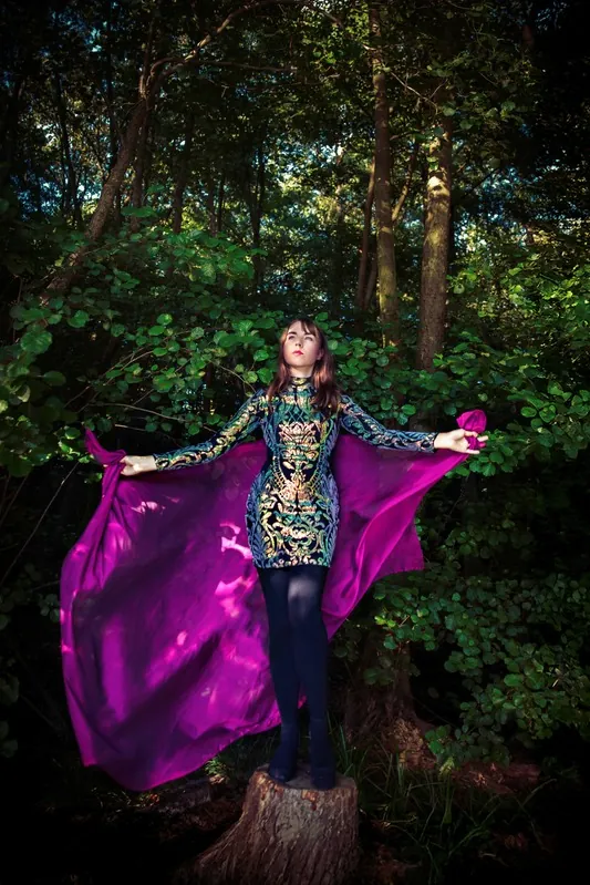 Vicky im Wald mit ausgebreitetem violettem Umhang
